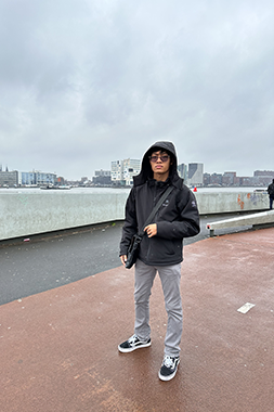 Preston wearing black rain coat standing in Amsterdam bay